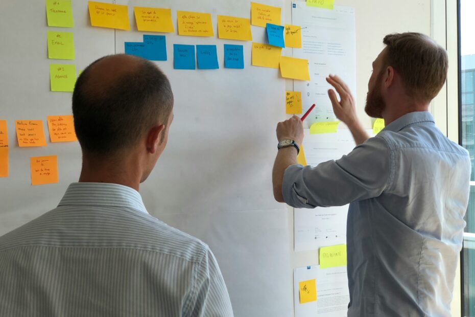 Two men in an office brainstorming, placing colorful sticky notes on a whiteboard planning virtual assistant onboarding